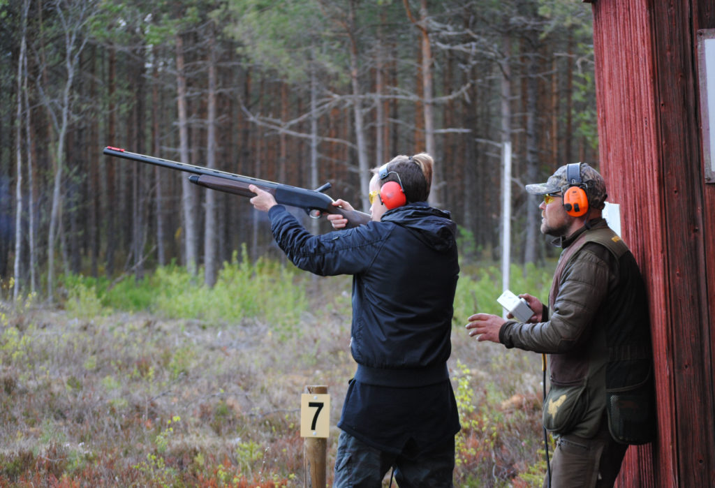 Tränaren övervakar praktikantens skytte med hagelgevär på skjutbanan.