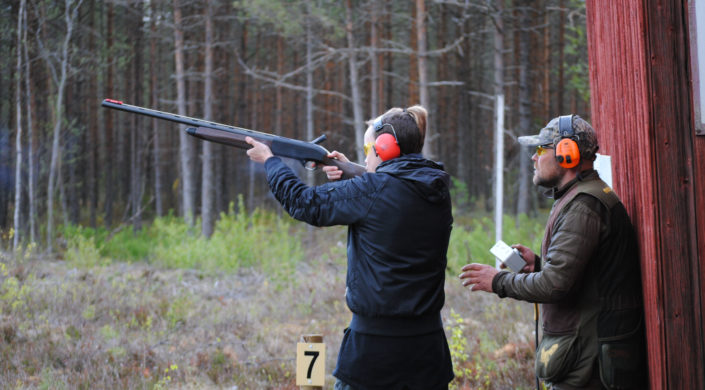 Kouluttaja valvoo harjoittelijan haulikkoammuntaa ampumaradalla.