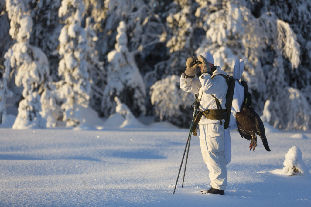 En jägare i en snödräkt tittar med kikare.