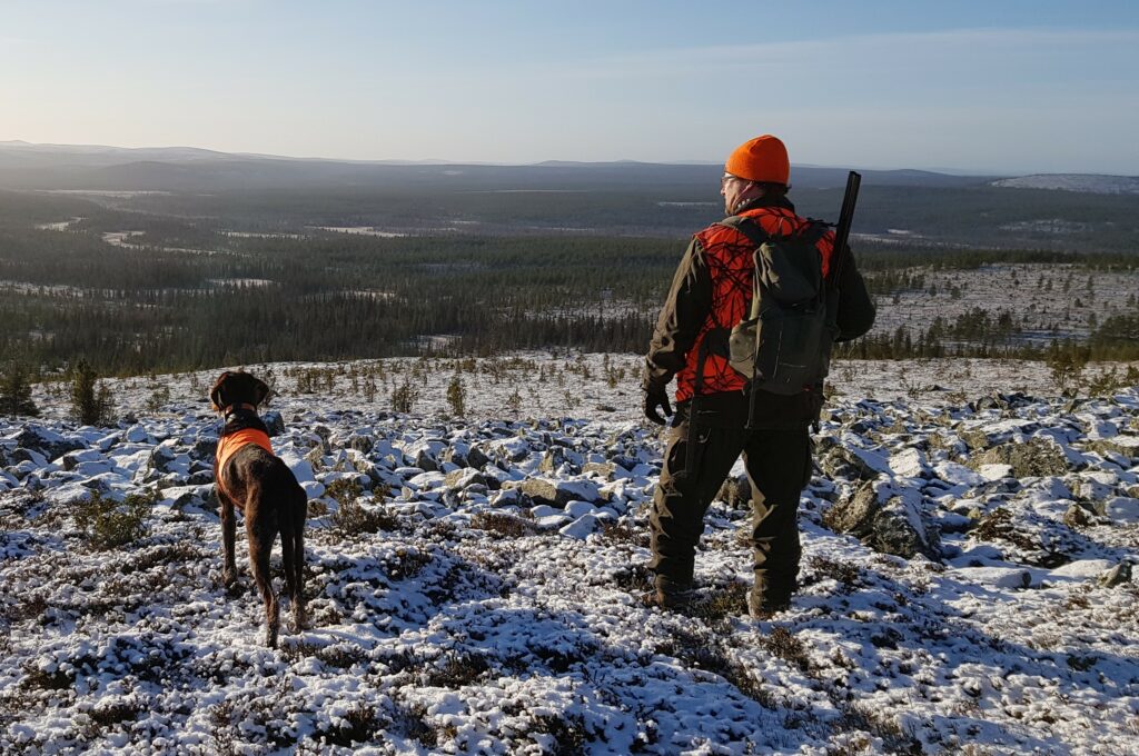 Mies ja saksanseisoja tunturissa huomiovärisissä asusteissa.