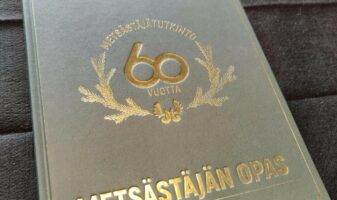 Metsästäjän oppaan 60 v. juhlaopas. Tekstit ja havuseppelelogo kullattuina.