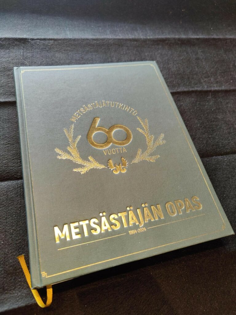 Metsästäjän oppaan 60 v. juhlaopas. Tekstit ja havuseppelelogo kullattuina.